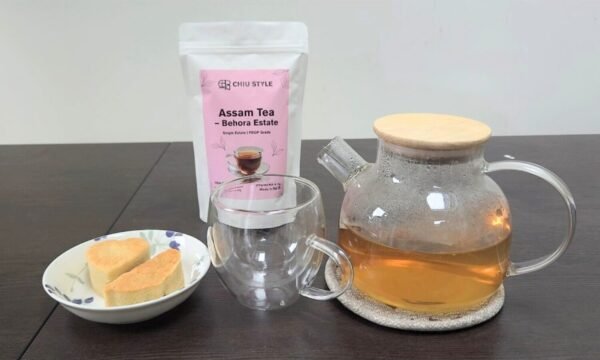 Glass teapot with freshly brewed CHIU STYLE Assam Black Tea, stand-up pouch of Assam Black Tea, and pineapple pastry on the side