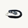 Angled side profile of the CHIU STYLE clover vegan leather braided keychain in classic black resting on a natural wood surface, highlighting texture and clover tag