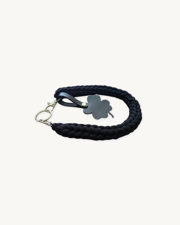 Angled side profile of the CHIU STYLE clover vegan leather braided keychain in classic black resting on a natural wood surface, highlighting texture and clover tag