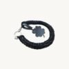 Angled side profile of the CHIU STYLE clover vegan leather braided keychain in black with silver thread resting on a natural wood surface, highlighting texture and clover tag