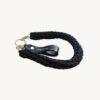 Angled side view of the black vegan leather braided keychain resting on a minimalist wooden table, showing the texture and hardware.