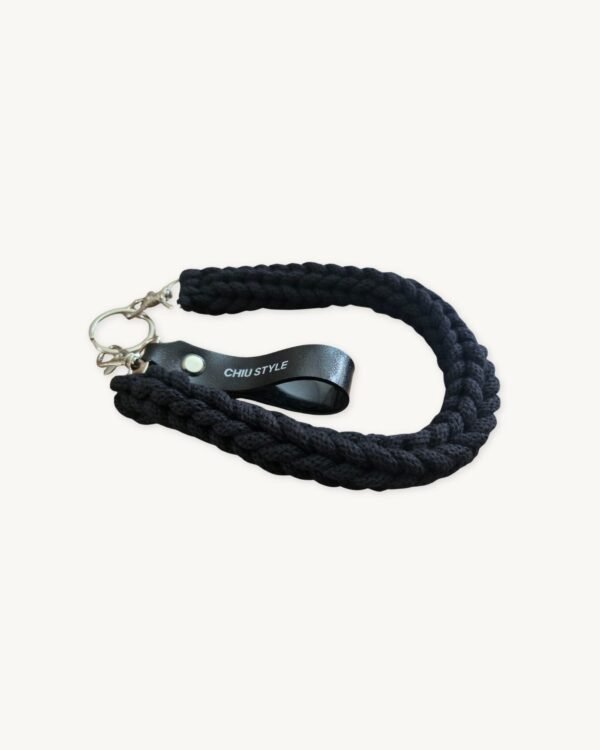 Angled side view of the black vegan leather braided keychain resting on a minimalist wooden table, showing the texture and hardware.