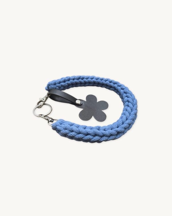 Angled side profile of the CHIU STYLE floral vegan leather braided keychain in Cornflowers Blue resting on a natural wood surface, highlighting texture and floral tag