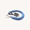 Angled side profile of the CHIU STYLE clover vegan leather braided keychain in cornflower blue resting on a natural wood surface, highlighting texture and clover tag