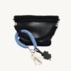 Cornflower blue clover vegan leather braided keychain looped around a tote bag handle, demonstrating easy key access inside a handbag