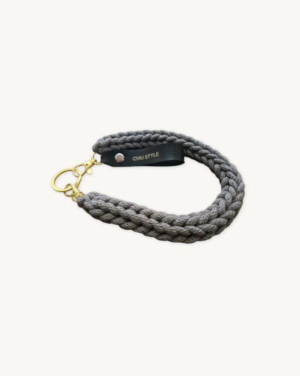 Angled side profile of the CHIU STYLE vegan leather braided keychain in Earth Mocha resting on a natural wooden surface, highlighting the texture and warm brown logo tag