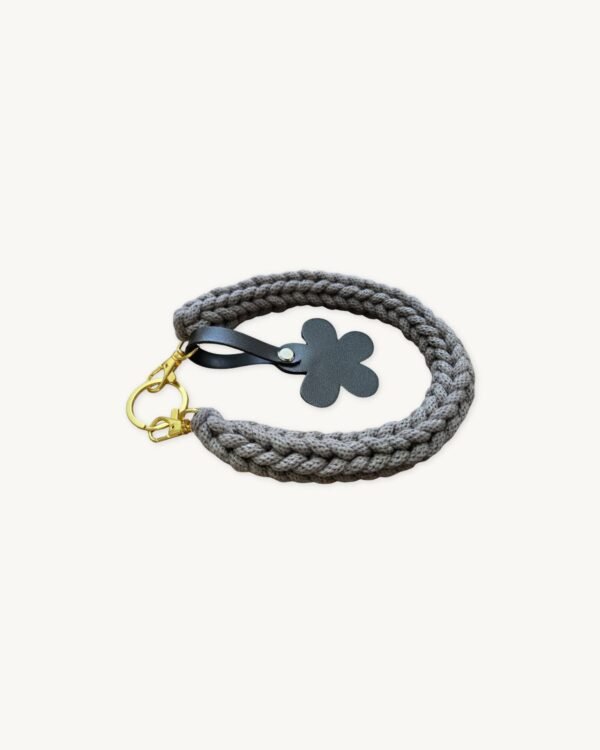 Angled side profile of the CHIU STYLE floral vegan leather braided keychain in mocha brown resting on a natural wood surface, highlighting texture and floral tag