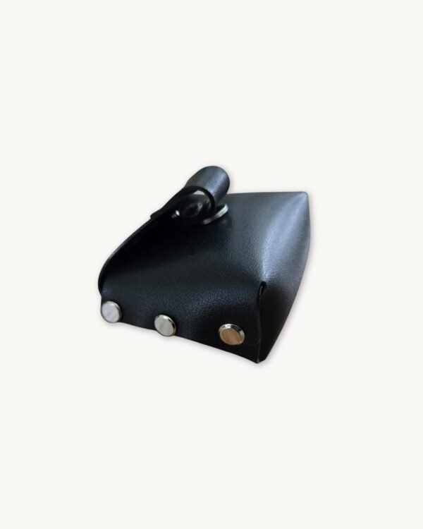 High-angle 3/4 view of the black minimalist vegan leather micro wallet, showcasing the top opening, side profile, and Chicago screw details.