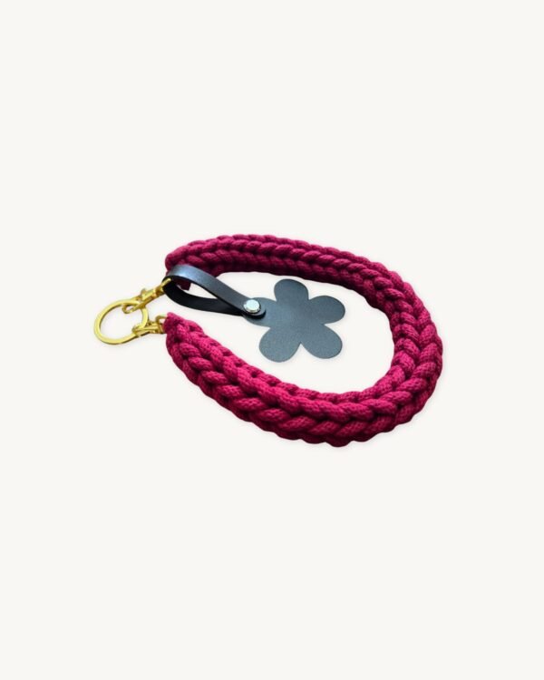Angled side profile of the CHIU STYLE floral vegan leather braided keychain in Sangria resting on a natural wood surface, showcasing texture and floral tag