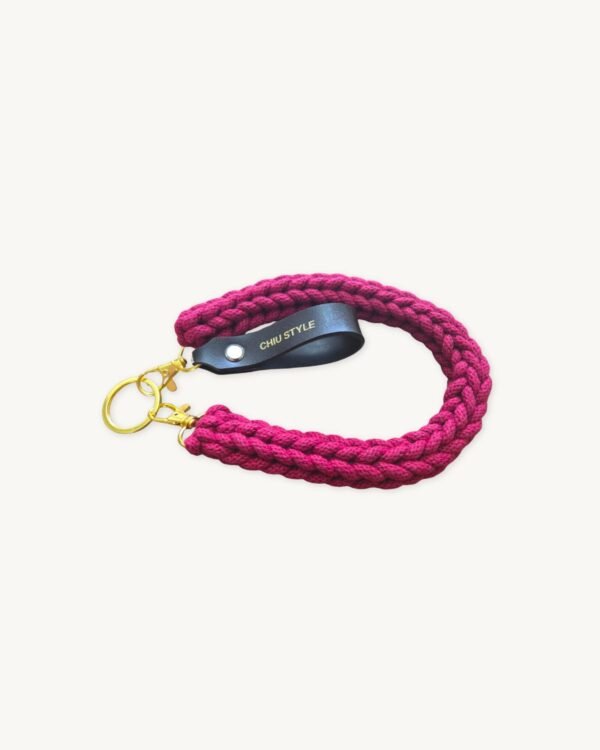 Angled side profile of the CHIU STYLE vegan leather braided keychain in Sangria resting on a natural wood surface, showcasing texture and warm brown tag