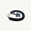 Angled side profile of the CHIU STYLE floral vegan leather braided keychain in Black with Silver Thread resting on a natural wood surface, highlighting texture and floral tag