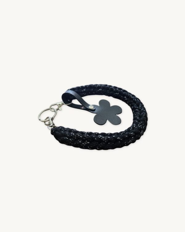 Angled side profile of the CHIU STYLE floral vegan leather braided keychain in Black with Silver Thread resting on a natural wood surface, highlighting texture and floral tag