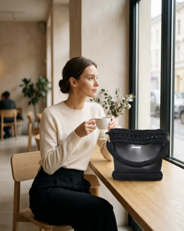 Lifestyle editorial photo of Vintage Punk Vegan Leather Laced Rhythm Handbag in black on a café table with a model holding coffee, showcasing crochet texture and draped handle